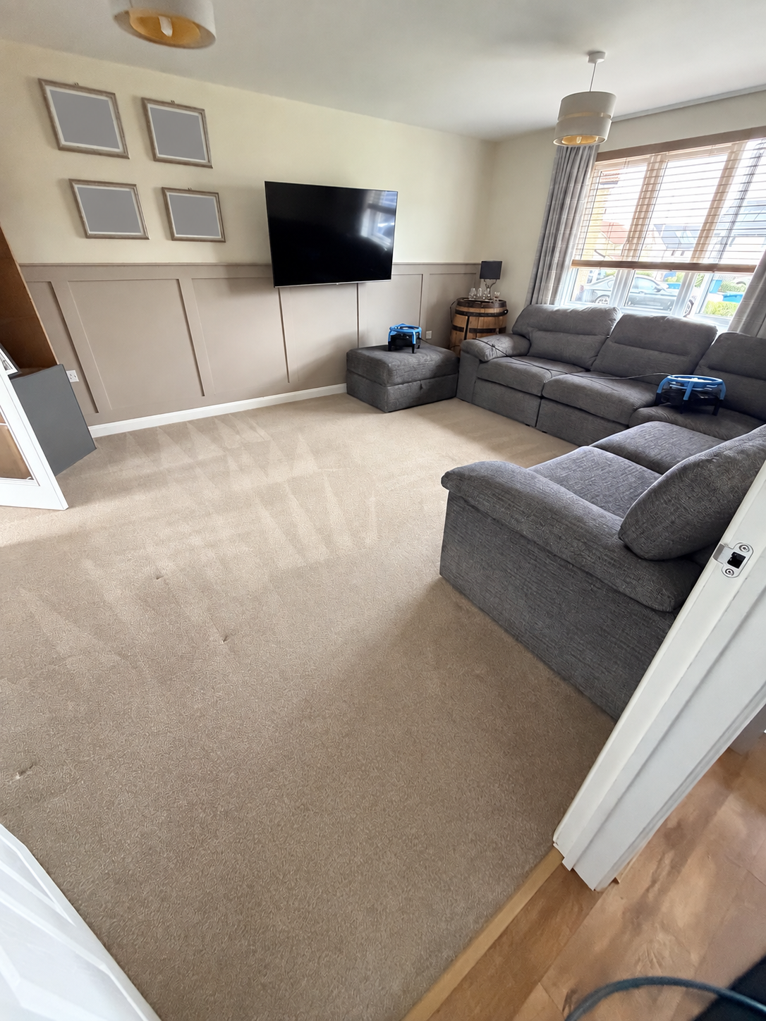 Cleaned grey corner sofa and beige living-room carpet in Calderwood, with family portraits obscured for privacy